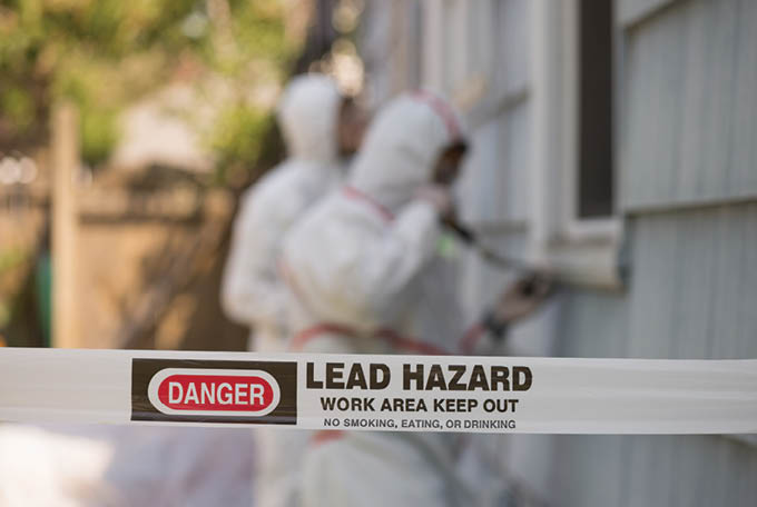 Two house painters in hazmat suits removing lead paint from an old house.