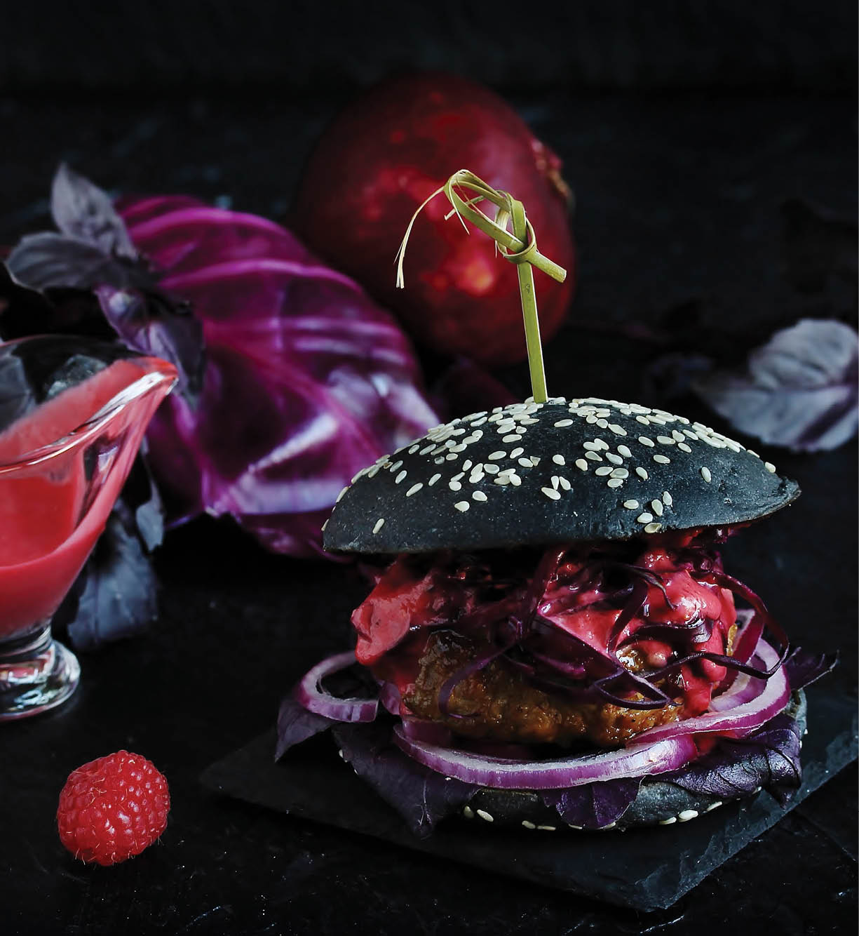 Black burger with raspberry homemade vinaigrette. On a dark background. Inside the cutlet, red onions, purple basil, red cabbage and raspberry homemade vinaigrette. An unusual combination.