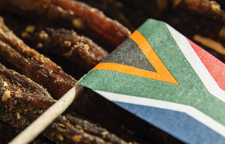 A close up image of a small South African flag on top of slices of biltong (cured meat) which is a traditional South African food snack. 